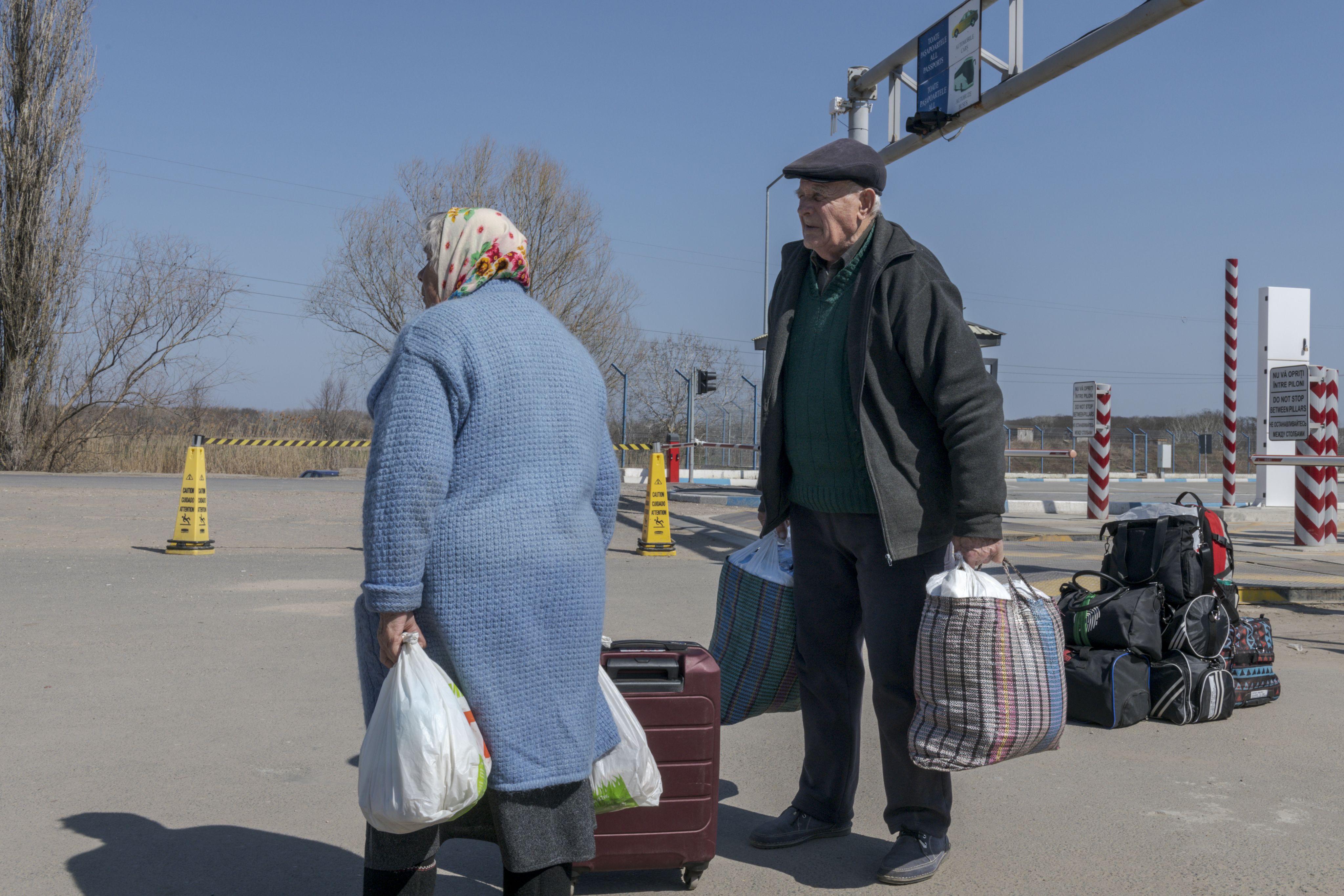 Older man and older woman with a few bags stood on a road. 