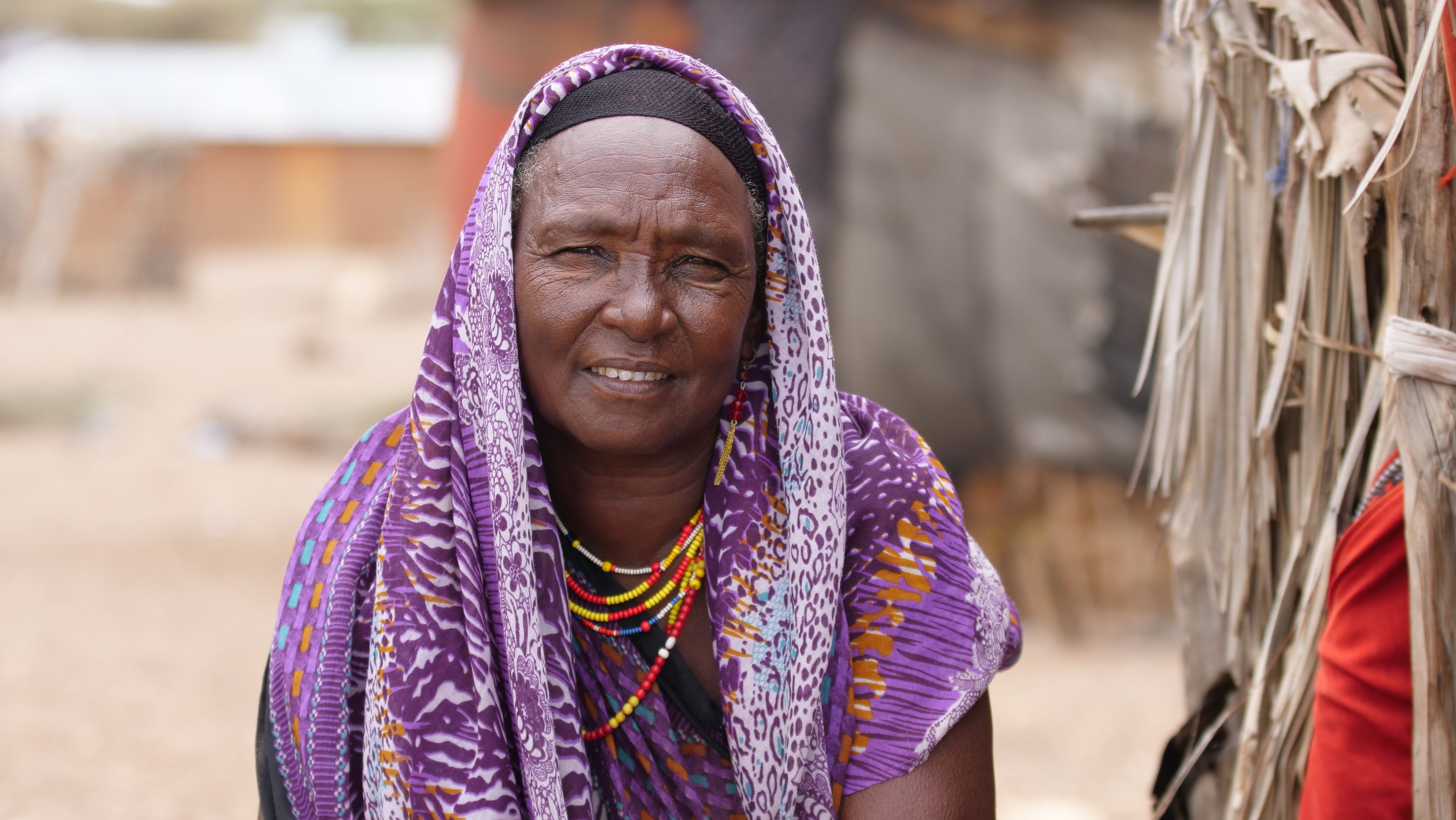 Female older person in front of huts during drought in South Sudan